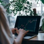 An individual analyzing stock market trends on a laptop in a cozy indoor setting with plants.