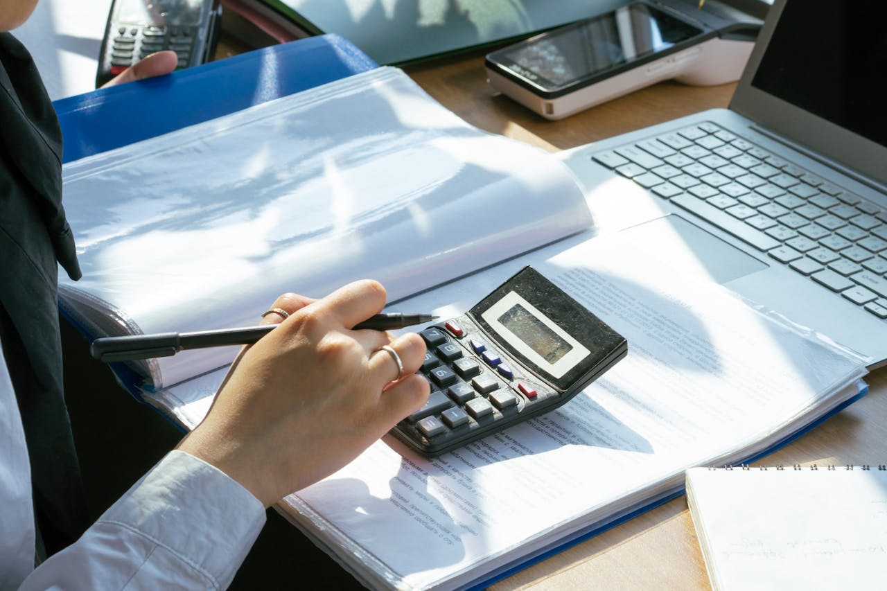 The Art of Drawing Readers In: Your attractive post title goes here A person working on financial calculations using a calculator and laptop at an office desk.